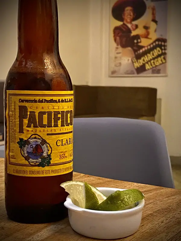 pacifico bottle of beer on table next to small cup with lemon slices