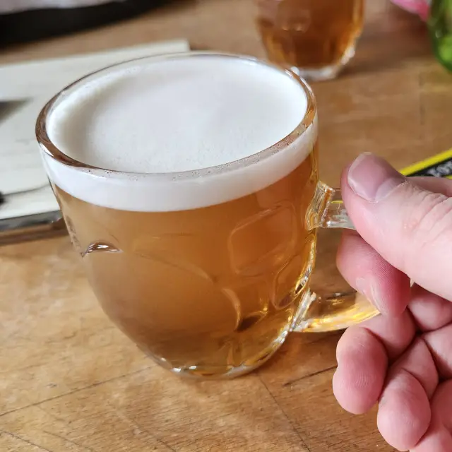 A hand holding an amber beer on the table.