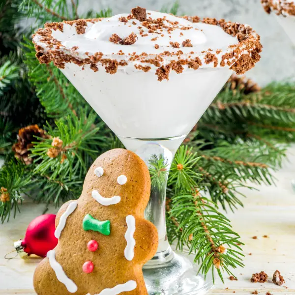 A close up of a Christmas Cocktail with a gingerbread man leaning on the glass.