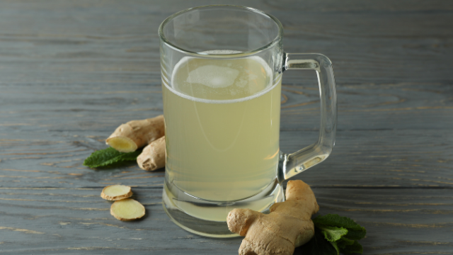 Ginger Beer In A Glass on a table surrounded by pieces of ginger.